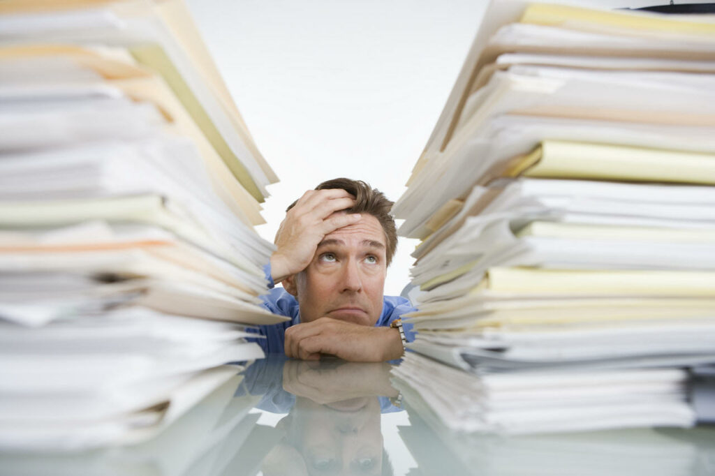 ManInMiddleOfPaperStacks Man Looking at Two Stacks of Paper
